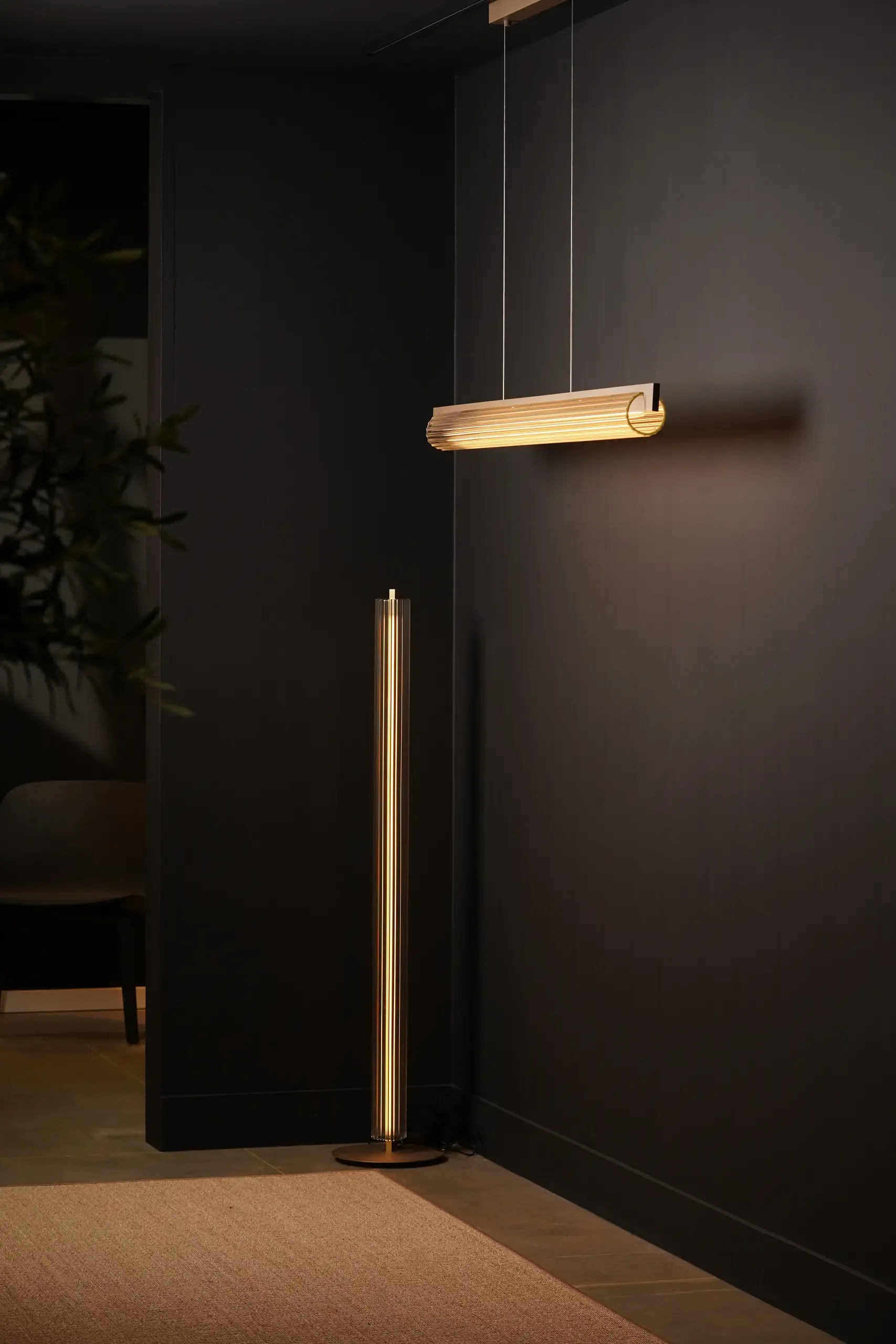 Lirra Floor und Lirra Pendelleuchte vor einer dunklen Wand
